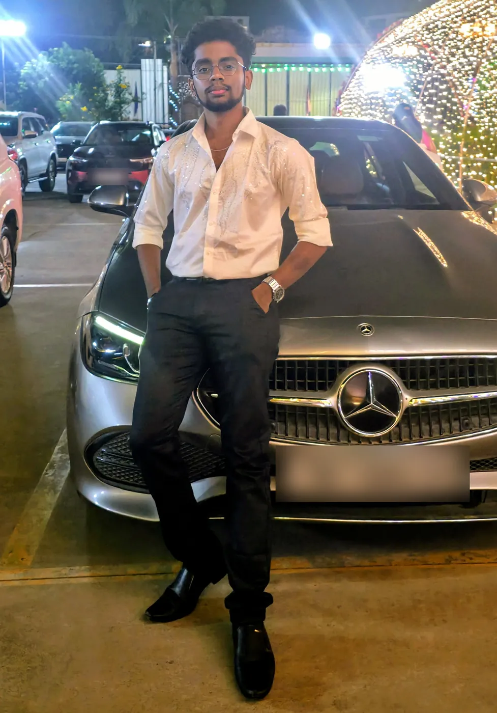 Darshan in a white shirt leaning on a silver car at night