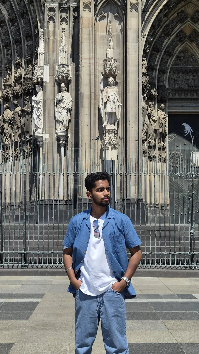 Darshan in a denim shirt in front of a gothic cathedral portal