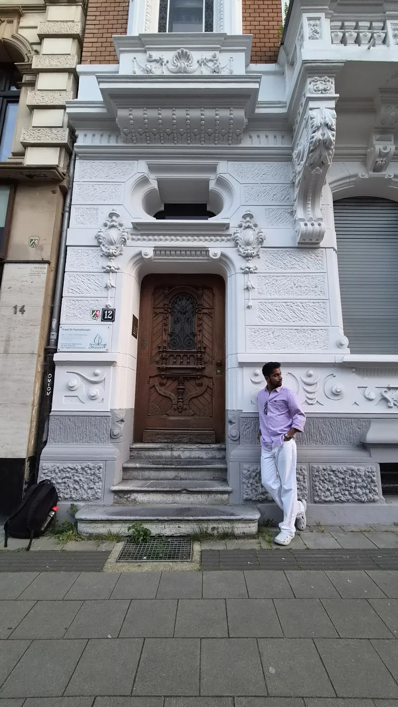 Darshan leaning against an ornate white facade