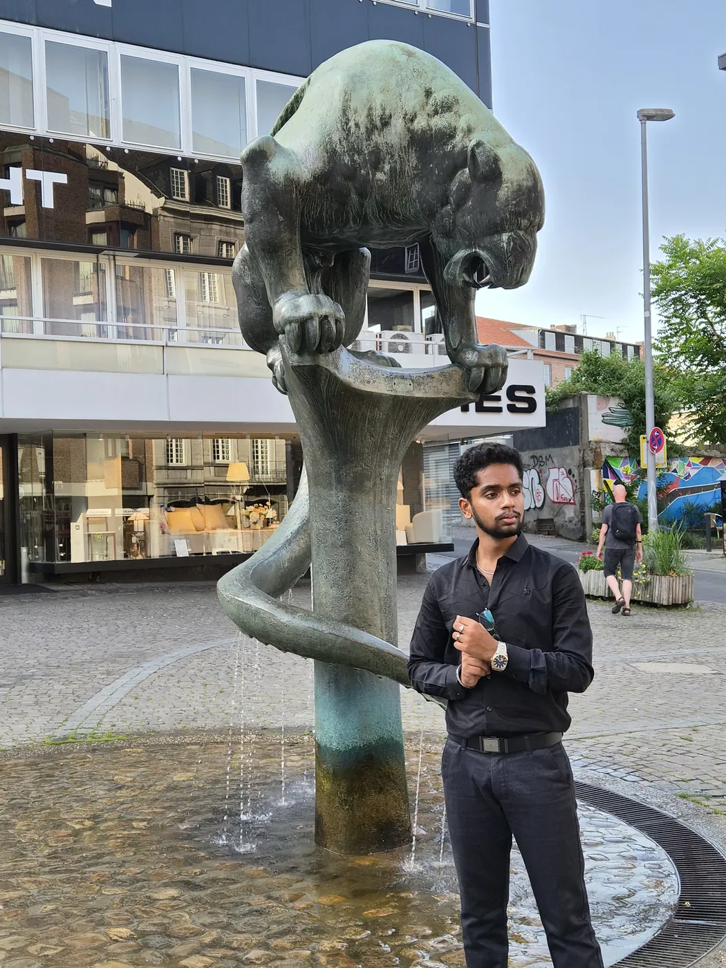 Darshan in black standing beside a bronze panther fountain