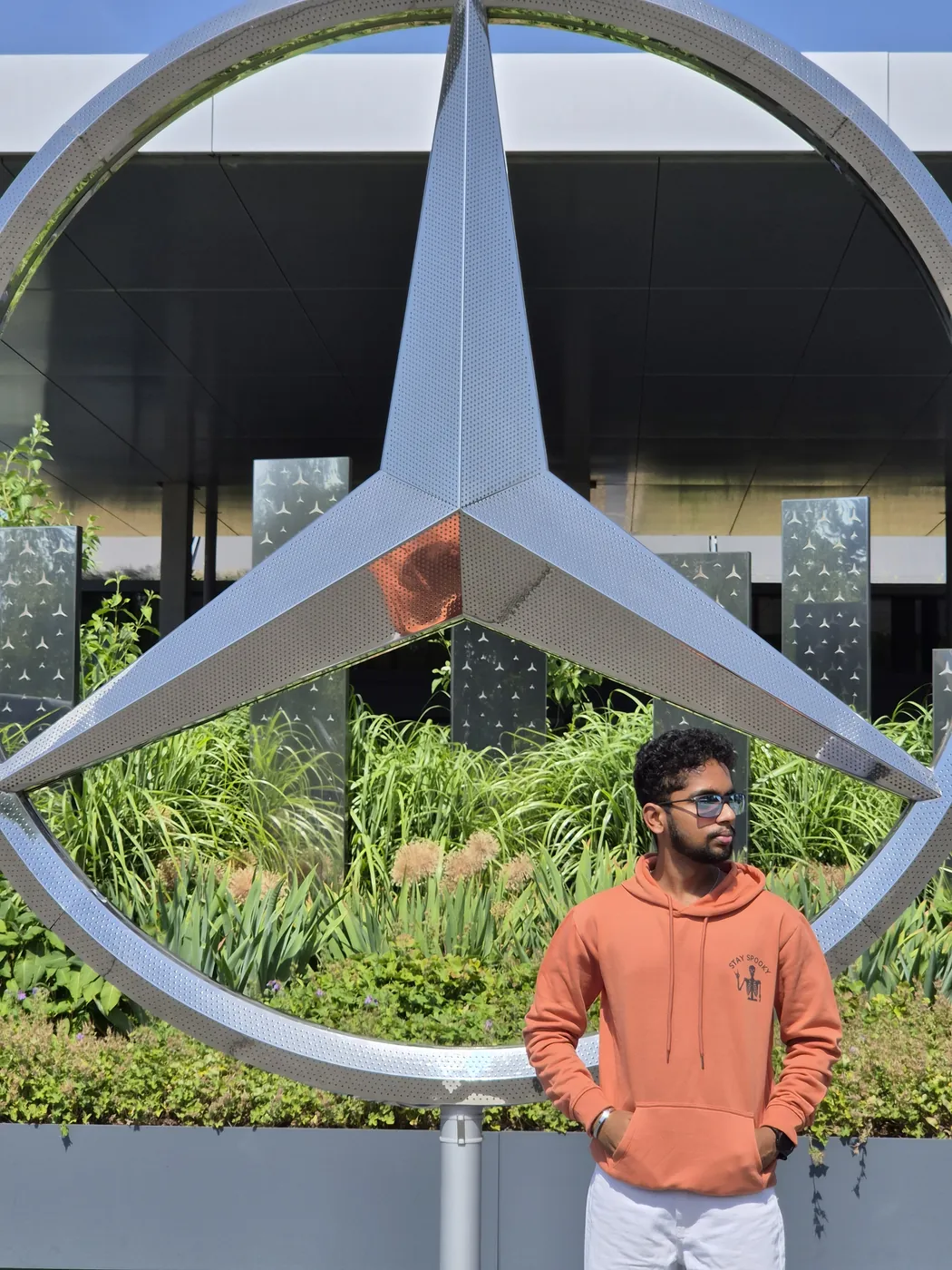 Darshan in an orange hoodie in front of a giant Mercedes-Benz star